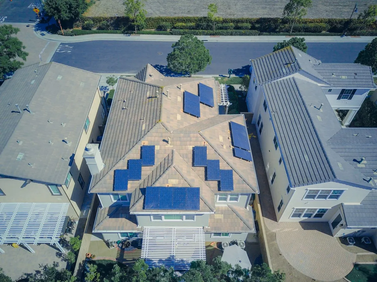Aerial view of a two-story suburban house with blue solar panels on a tile roof, between two neighboring homes