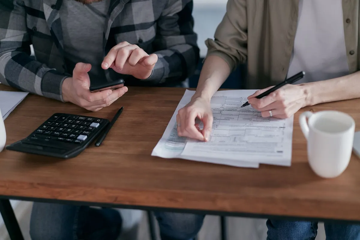 A couple at a wooden table with a calculator, a pen and printed tax paperwork