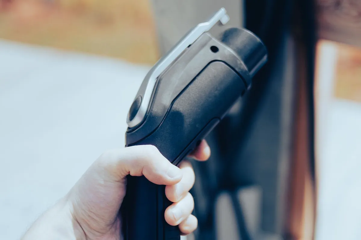 Hand holding an electric car charging connector next to a wall-mounted home charger