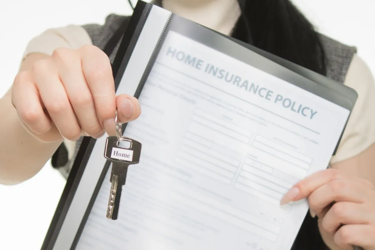 Hand holding a house key next to a home insurance policy form