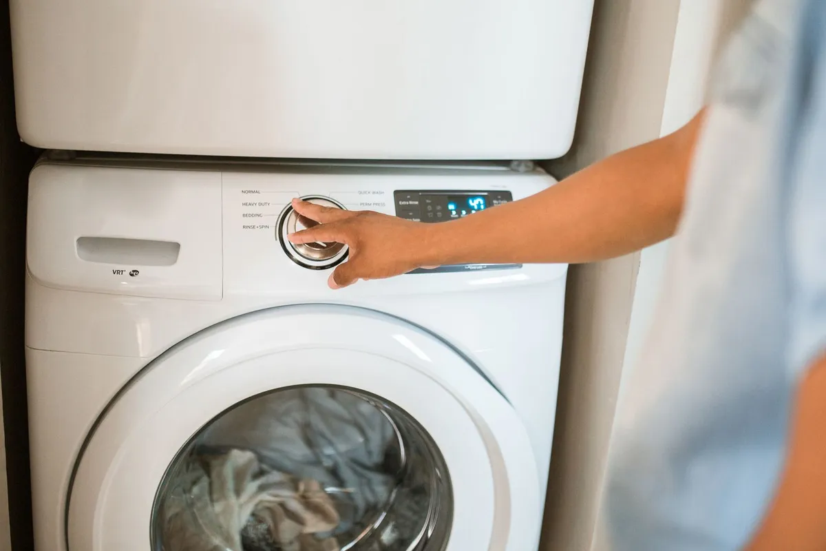 Hand turning the cycle dial on a white front-load dryer with clothes visible inside