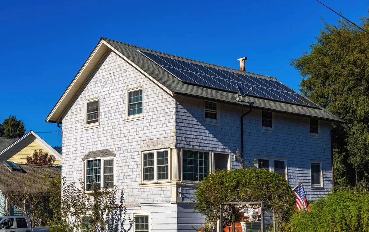 Two-story white house with a row of solar panels on the roof under a clear blue sky