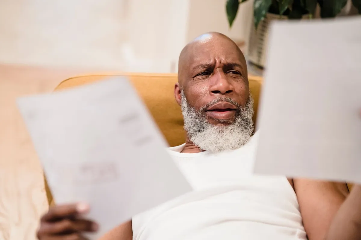 Man with a gray beard squinting at the pages of a utility bill he holds in both hands