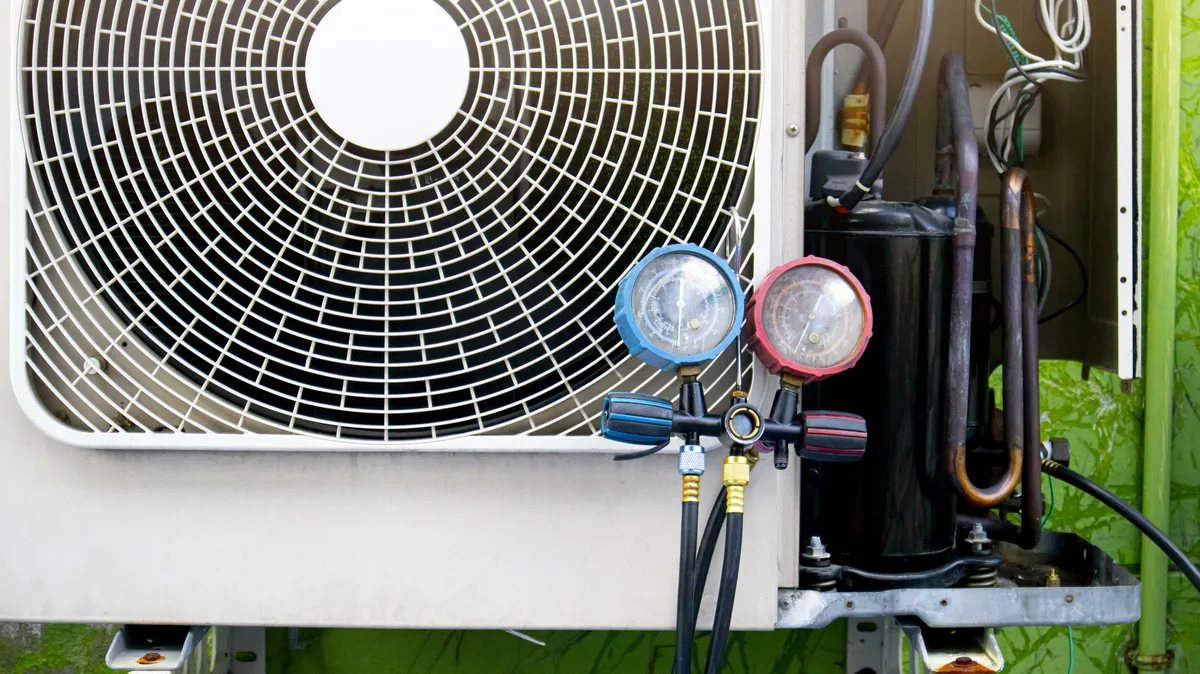 Blue and red refrigerant gauges hanging on the fan grille of an outdoor unit with its compressor and copper tubing exposed