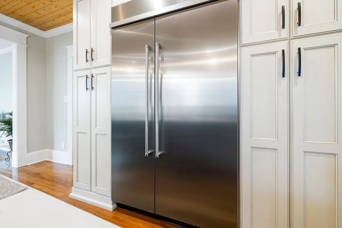 Tall stainless steel refrigerator with two doors built into white kitchen cabinets