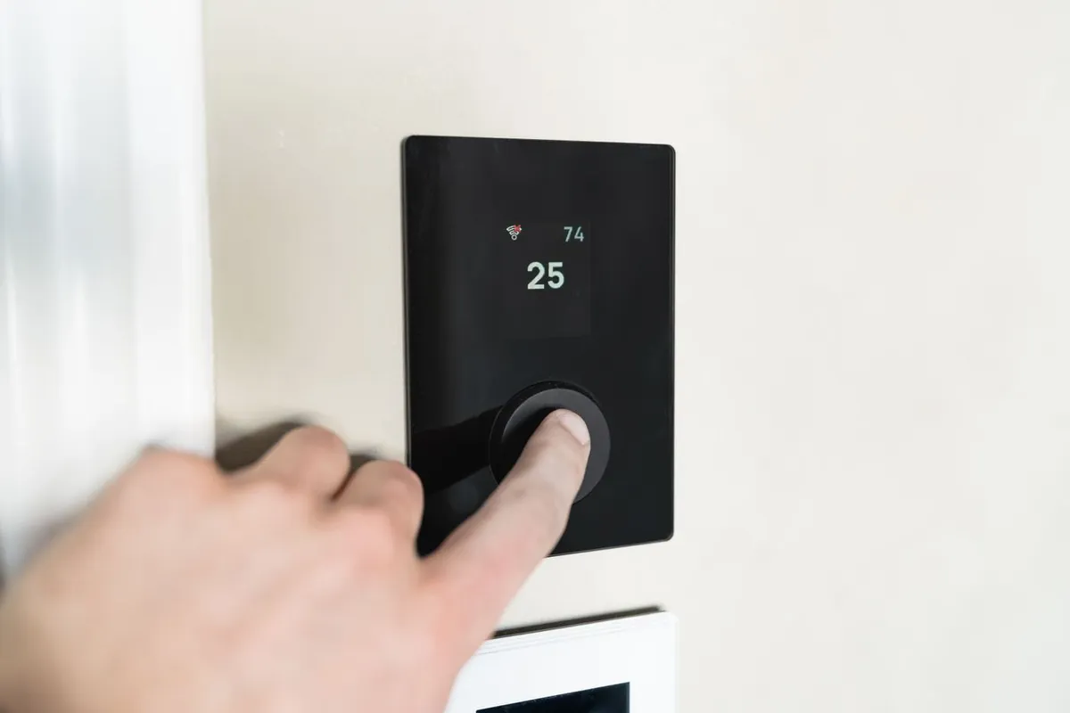 Hand pressing the dial of a wall-mounted digital thermostat in a home